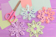 Pink, purple, blue, green paper cut snowflakes, stationery craft supplies on wood background. Merry Christmas paper snowflakes cutouts craft art. Winter diy projects for kids