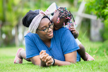 Wall Mural - Cheerful african american girl playing on the back of her mother, Happy mother and daughter laughing together outdoor