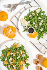 Sticker - Arugula salad with gorgonzola cheese, tangerines, walnuts, and balsamic vinegar. Arugula and cheese salad in white plates on a white background top view. Light and healthy food.