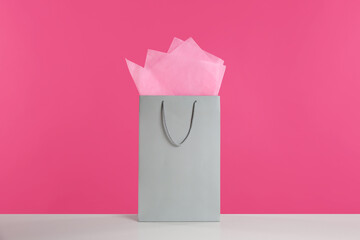 Gift bag with paper on white table against pink background