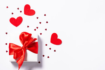 Wall Mural - St. Valentine’s Day card concept. White gift box with big red bow and shining heart-shaped decorations on white background with copy space for your text.