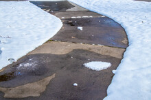 Close-up Of Curving Residential Sidewalk Cleared Of Snow, But With Spots Remaining And Large Wet Areas.