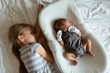 Little sister and her newborn brother. Toddler kid meeting new sibling. Cute girl and new born baby boy relax in a home bedroom. Family with two children at home. Love, trust and tenderness concept