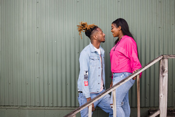 An attractive African-American teenage couple spending time together outdoors in an urban setting of a green old warehouse metal building