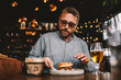 © dusanpetkovic1 - Middle aged bearded hungry man sitting in restaurant and eating delicious burger.