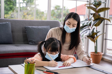 Home schooling learning at home during virus pandemic. asian woman with her daughter in the living room , wearing surgical face masks to protect them from the virus.