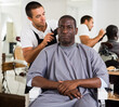 © JackF - African male client getting haircut at barber shop from professional hairstylist using clipper