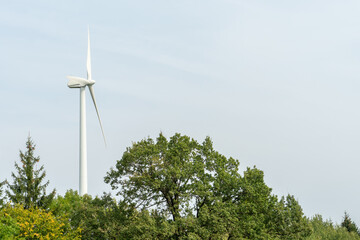 view of a modern windmill against a blue sky. The white blades of the wind turbine. Wind turbines in the forest away from the big city on a summer day. Clean and renewable energy production