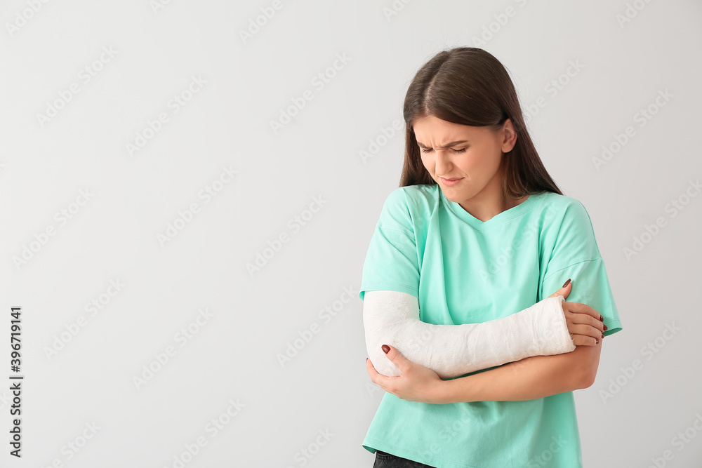 Young woman with broken arm on light background