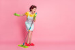 Full length body size view of nice ecstatic cheerful housemaid singing hit song using besom like mic isolated pink color background