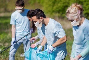 Poster - volunteering, health and ecology concept - group of volunteers wearing face protective medical mask for protection from virus disease with garbage bags cleaning area in park