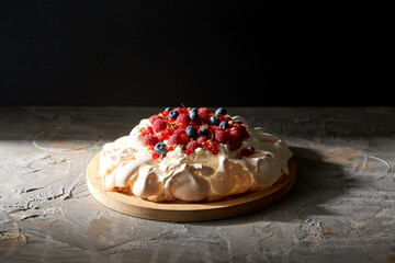 Wall Mural - food, culinary, baking and cooking concept - close up of pavlova meringue cake decorated with berries on wooden serving board