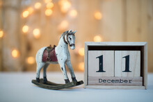 Cube Wooden Calendar Showing Date On 11th December With Old Toy Rocking Horse Over Bokeh Background. Advent Calendar, Christmas Background, Copy Space