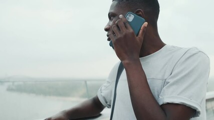 Poster - A pleased african american man is talking on his smartphone standing outside in the city