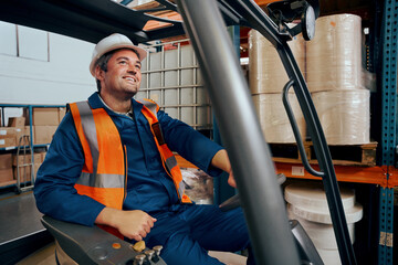 Happy engineer operating forklift truck in warehouse