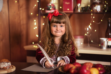 Wall Mural - girl with cake. Little girl writes a letter to Santa Claus. A child near the Christmas tree. Happy child smiles. Girl with long curly hair