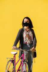 Wall Mural - girl wearing mask walks with bike in a yellow wall