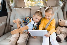 Smiling Girl Holding Digital Tablet Near Brother With Toy Plane In Car
