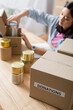 © LIGHTFIELD STUDIOS - Box with donations lettering near canned food and asian volunteer on blurred background