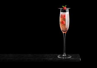 Elegant glass of pink rose champagne with raspberries inside on black marble board on black background.Space for text