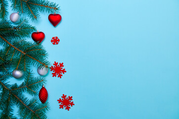 Christmas composition of fir branches, red heart and Christmas decorations on a blue background. View from above. Postcard for the New Year.