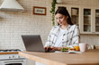 Beautiful pleased woman working with laptop while having breakfast