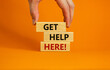 Get help here symbol. Male hand builds stack from blocks with words 'get help here'. Beautiful orange background. Copy space. Business and get help here concept.
