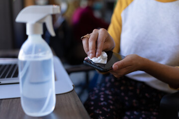 Wall Mural - Mixed race woman disinfecting her smartphone in an office