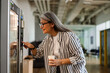Happy white-haired woman using vending machine while drinking coffee