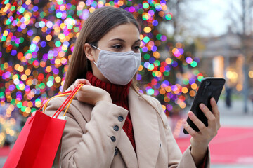 Wall Mural - Happy woman with face mask reading text on smartphone in Christmas time