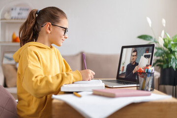 Wall Mural - School girl having video conference with online teacher on laptop in living room at home. Homeschooling, distance learning, online education due to coronavirus pandemic. Side view. E-learning concept