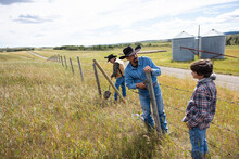 Multigenerational Male Ranchers Fixing Barbed Wire Fence On Ranch