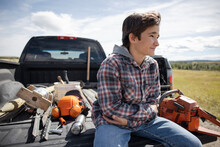 Boy Sitting In Pickup Truck Bed With Tools On Sunny Rural Farm