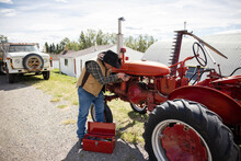 Senior Farmer In Cowboy Hat Fixing Tractor On Sunny Rural Farm