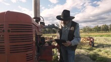Senior Male Farmer With Digital Tablet Fixing Tractor In Sunny Farm Fi