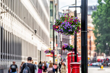 London, UK Buildings And Hanging Flower Baskets With People In Blurry Background On Street Road In Summer With Colorful Flowers