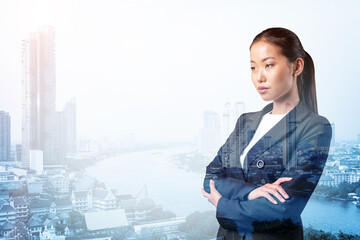 Prosperous Asian businesswoman in suit in crossed arms pose. Bangkok cityscape. The concept of woman in business. Financial downtown. Double exposure.