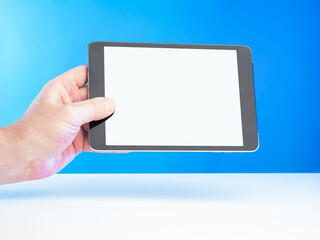 Poster - A man's hand holds a horizontal digital tablet. An electronic tablet with a blank screen. Electronic gadget on a blue-blue background. Space for your text on the tablet screen.