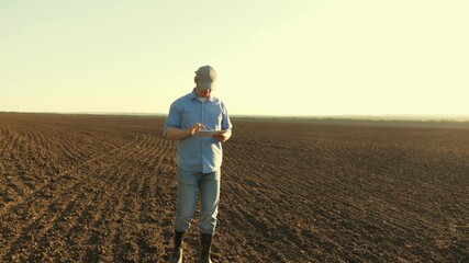 a farmer works with a tablet in a plowed field in sun. agronomist with a tablet studying the harvest