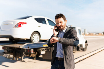 Latin man talking and looking at his watch next to a tow truck