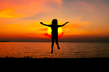 Wall Mural - Silhouette happy young girl jumping cheerful on sand near beach with beautiful sunset sky background.