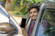 © PRASANNAPIX - Young Indian businessman sitting in side of car and showing smart phone screen