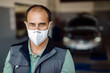 Mid adult mechanic wearing protective face mask in a workshop and looking at camera.