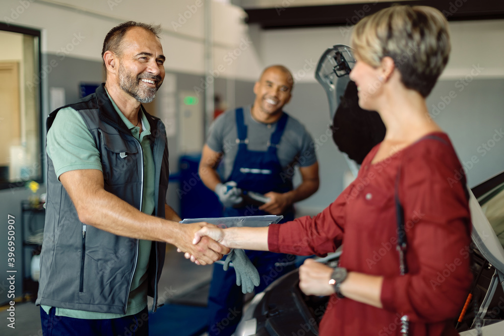 Happy mechanic handshaking with female customer in auto repair shop.