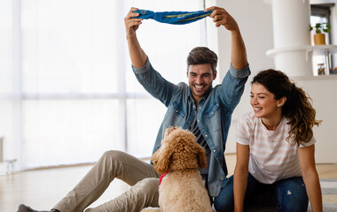 Wall Mural - Cheerful young loving couple is playing with their dog at home.