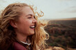© StratfordProductions - Closeup of a laughing young woman enjoying windy breeze touching face with hair flying while looking away - the feeling of freedom in nature