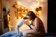 © natalialeb - Caucasian Child with puppy on the background of a Magic Homemade Advent calendar on a tree branch on the wall of the house, festive decor and tasks for children, garland lights