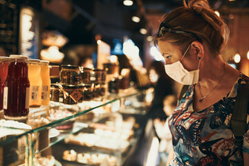 Young woman shopping in grocery store in the evening, wearing the face mask to avoid virus infection and to prevent the spread of disease in time of coronavirus