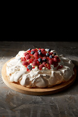 Wall Mural - food, culinary, baking and cooking concept - close up of pavlova meringue cake decorated with berries on wooden serving board