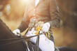A rider sitting in the saddle on a black horse is holding a bridle rein and a bouquet of summer field herbs in the sunlight. A cute gift at an equestrian competition. Horseback riding.